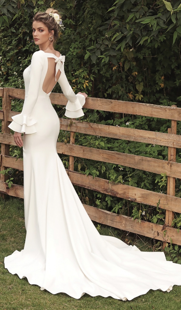 Alia by Chic Nostalgia Alia is meticulously crafted into a classy scoop neckline, a bow-knotted open back, concise long sleeves with layered flare cuffs, and a flowy crepe mermaid skirt. MJ Bridal Collection, price available upon request.