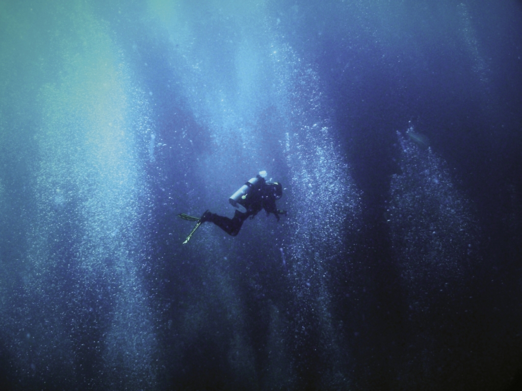 A diver to the SS Hebe descends through the blue void and a cloud of bubbles exhaled by divers already on the bottom.