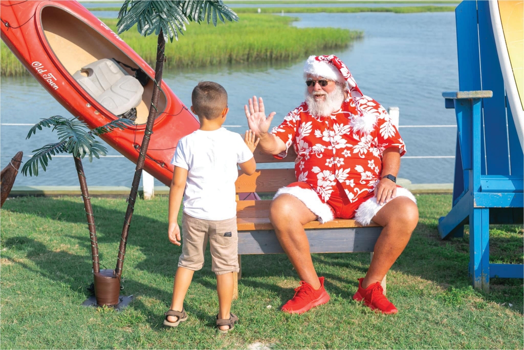 Santa Greg  Greg Calvert, aka Santa Greg, first dressed up for fun as Kris Kringle for the Murrells Inlet MarshWalk’s Santa Crawl in 2017. You can now find him in his sleigh every year during the MarshWalk Wonderland of Lights and at many other venues; Summer Santa Greg high- fives a boy at a photo shoot.