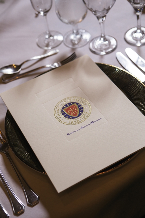 The Table Is Set: A formal program at each place setting introduces the guests for the evening and gives details of each food course and wine to be served. At right, middle photo, from left: Chaîne Officier Bonnie Fisher (with ribbon),Chevalier Rick Fallon, Dame de la Chaîne Sharon Fallon.