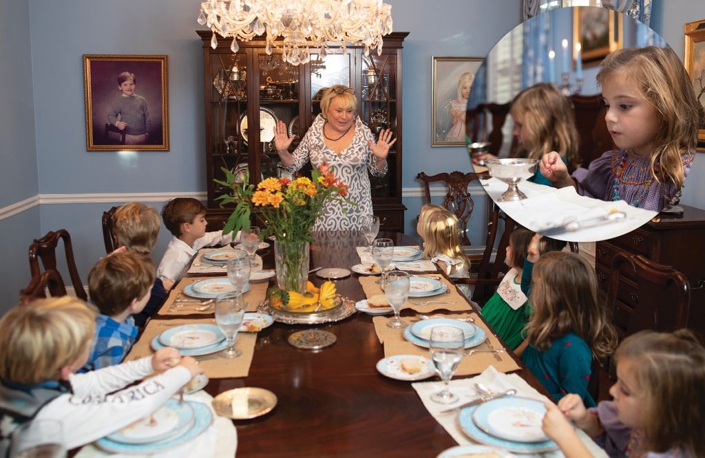 Ms. Flo talks to manners campers while they sit in her dining room featuring family portraits and a polished mahogany dining table.