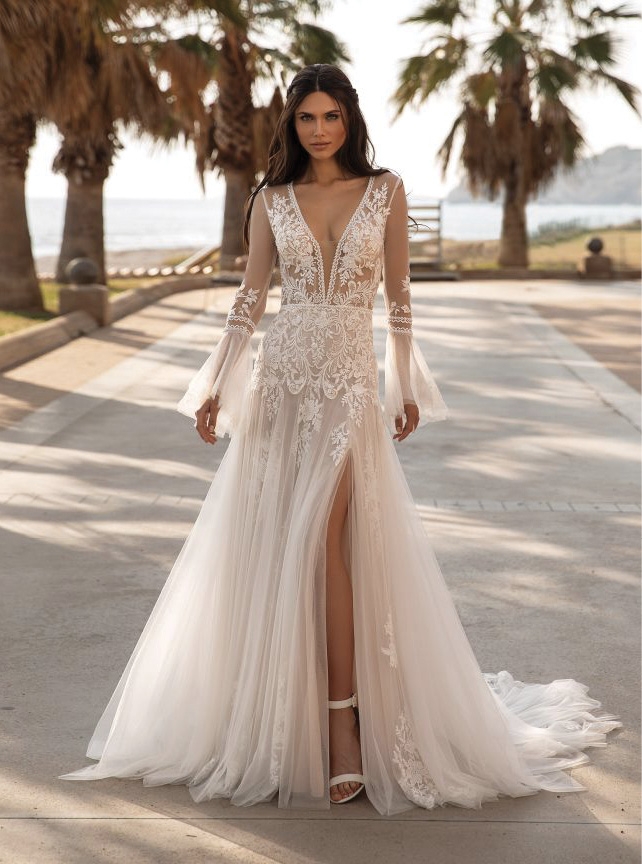 PRONOVIAS TYSON - Glide through your wedding day in this whimsical wedding dress fashioned from lace and tulle. With long bell sleeves, split evasé skirt and a chapel train creating a unique vision of ethereal elegance. MJ Bridal Collection; Prices available on request
