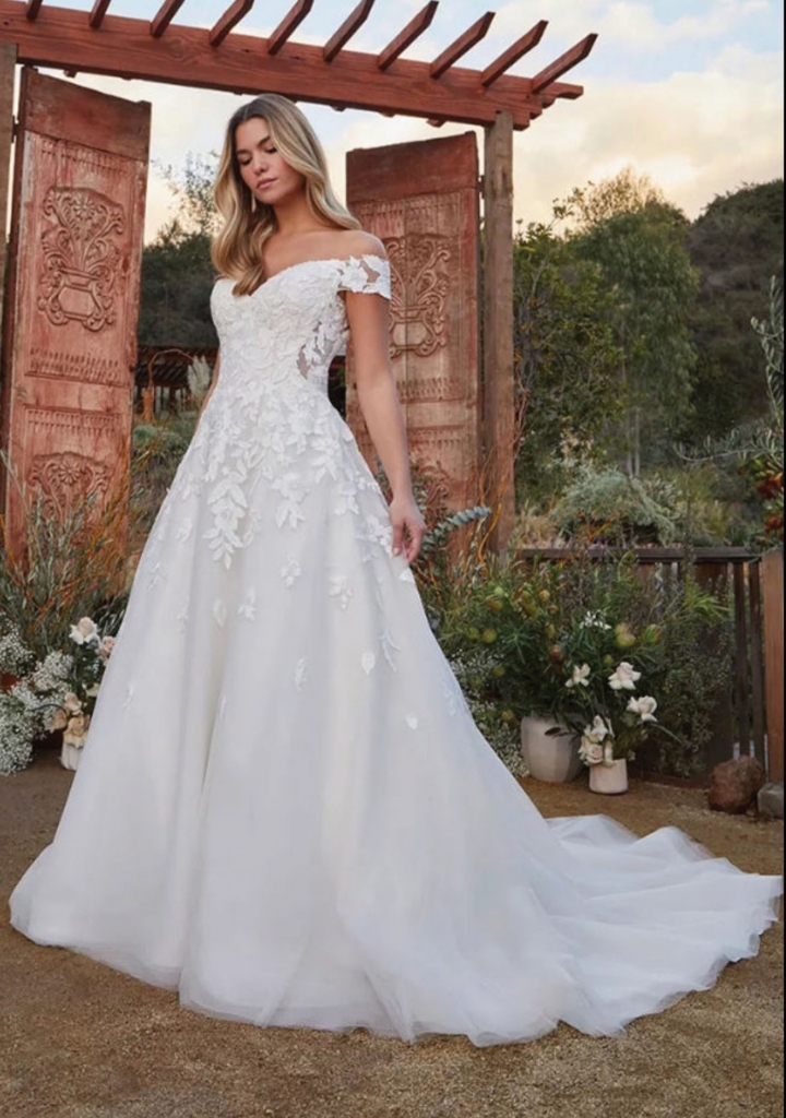 Beloved by Casablanca - Bodhi style BL419  A-line shape is crafted with layers of lining, shimmer tulle, and sequined floral lace appliques. An off-shoulder neckline shape with a micro subtle plunge and curved lined bodice. Lace appliques continue down the skirt with a 73” train. Irresistible Elegance, $1,500