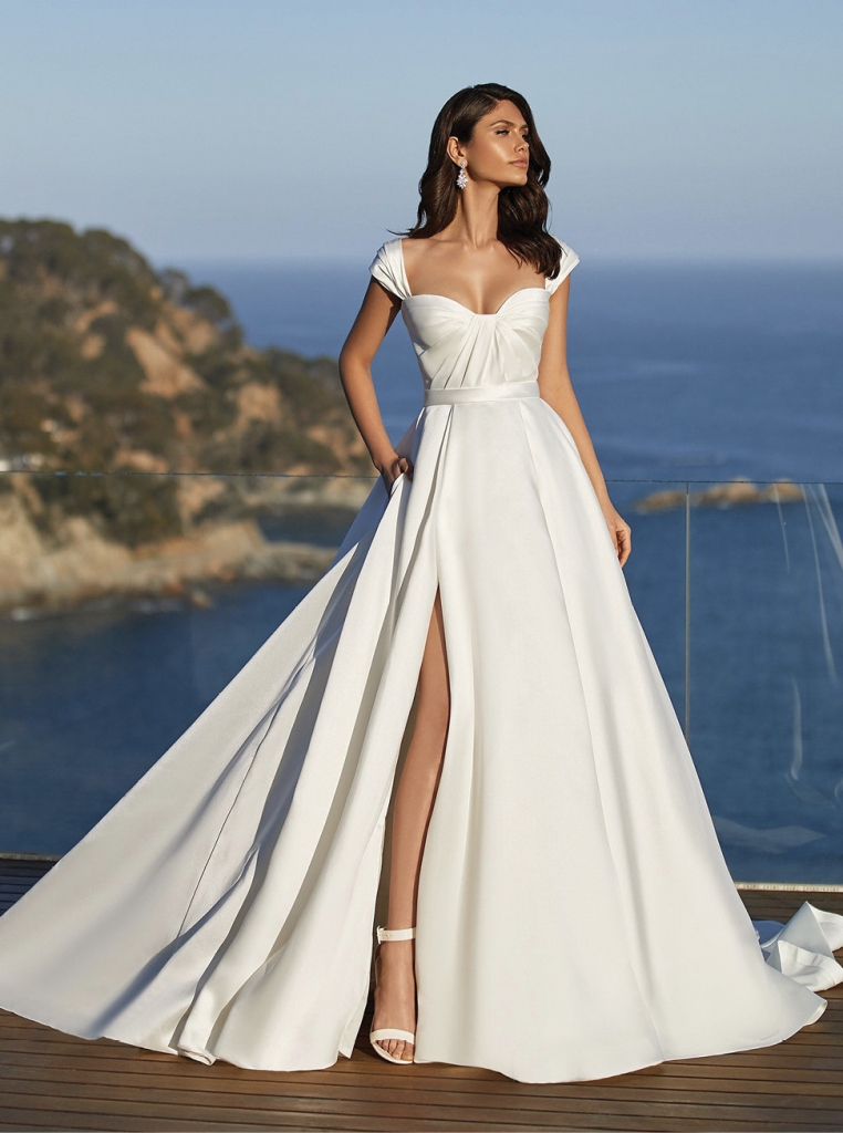 Dominique by Pronovias For screen-inspired glamor, this Mikado gown has a draped sweetheart bodice with detachable cap sleeves, and a full-blown skirt with a daring front split. Two Oaks Bridal, contact for pricing.
