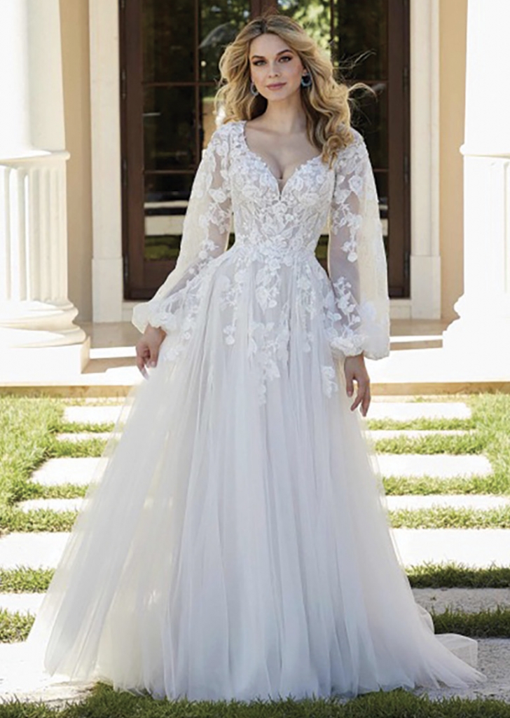 Felista by Morilee The soft net floats in this relaxed ballgown, with crystal beaded frosted lace appliqués. Gauzy bishop sleeves and a keyhole back create a boho vibe and the lace-trimmed train adds a bit of  romance. Shown in Ivory/Almond/Honey. The Foxy Lady, $1,599