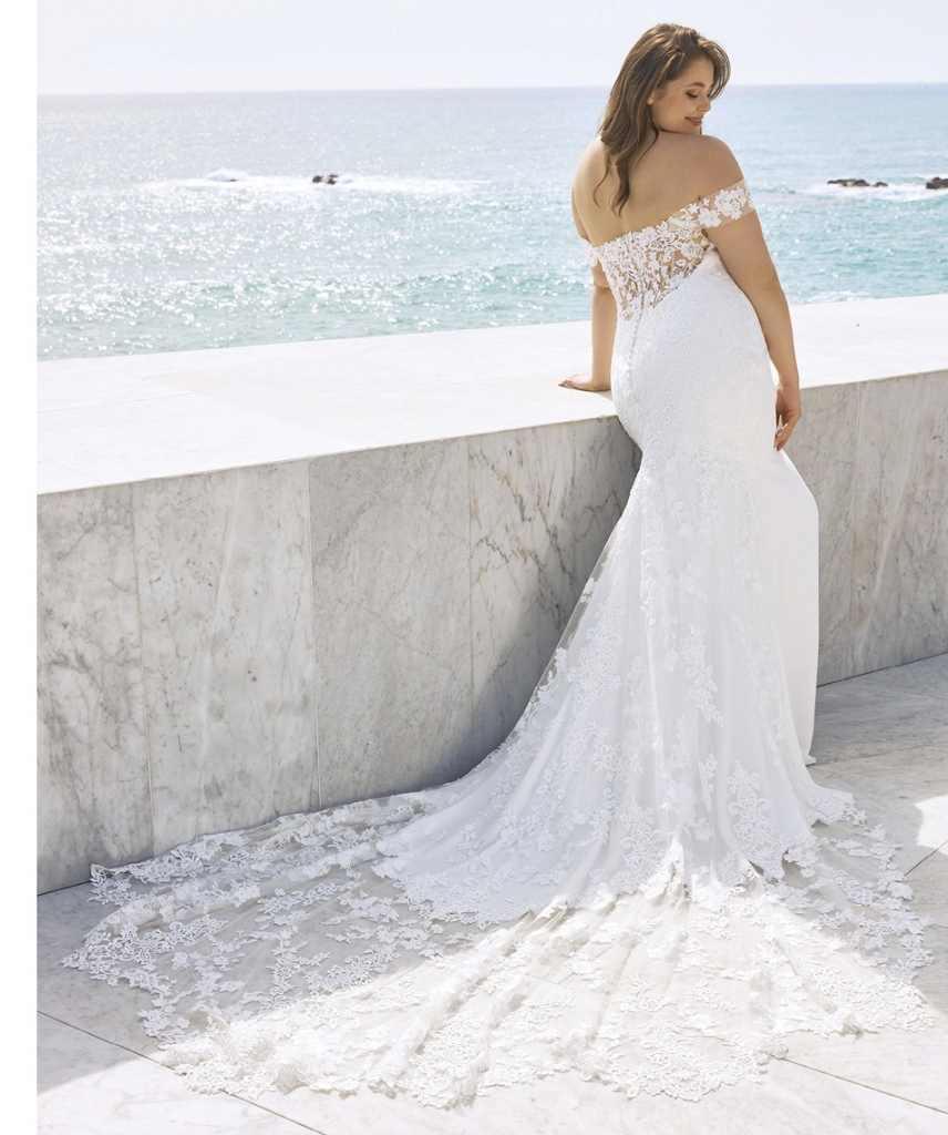 Syrinx by Pronovias White petals flutter about the off-the-shoulder sleeves of this strapless, crepe wedding gown, whose clean, white facade juxtaposes with a full back and train adorned in floral lace placements. Two Oaks Bridal, contact for pricing.